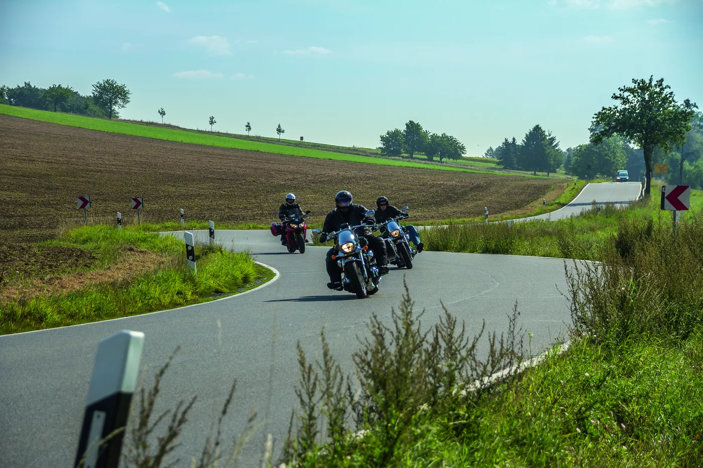 Mehrere Motorräder auf einer geschwungenen Landstraße durch Felder Mehrere Motorräder auf einer geschwungenen Landstraße durch Felder